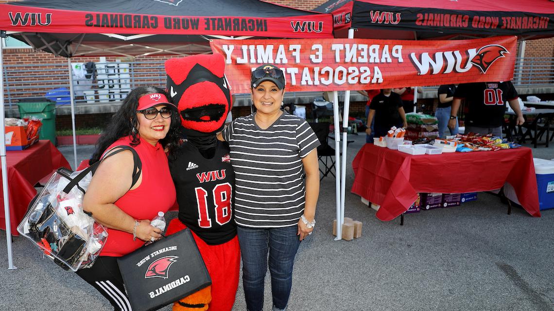 Red the Cardinal poses with two UIW alumni outside the parent and family area on campus